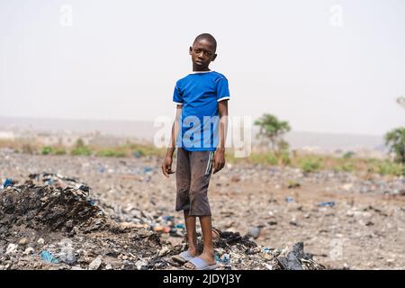 Desperate African boy with stands sadly in the middle of a garbage field, symbolizing the environmental problems caused by improper garbage disposal a Stock Photo