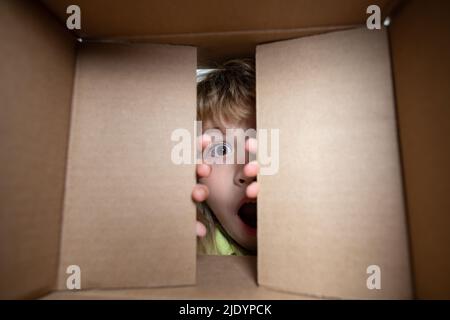 Child boy opening a carton box and looking inside, unpacking concept, surprise unboxing. Child with open box. Stock Photo