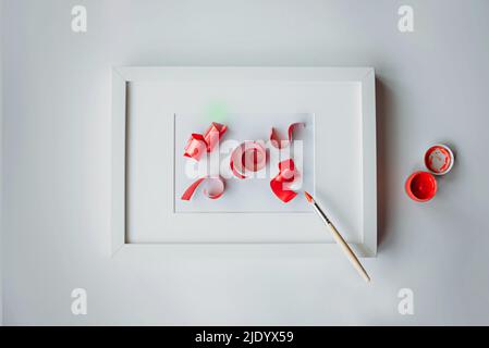 A frame with a passe-partout and a levitating brush draws 3D ribbons with red paint. Stock Photo