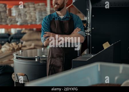 Unrecognizable worker in uniform standing on warehouse of small coffee factory Stock Photo