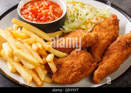 Serbian fried chicken with French fries, cabbage salad and hot sauce close up in the plate on the table. Horizontal Stock Photo