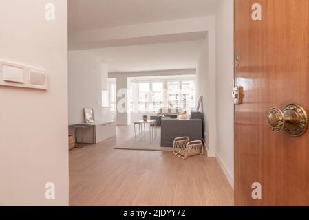 entrance hall of a house with light wooden door, light oak flooring, large window in the background and plain white painted walls Stock Photo