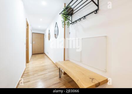 Entrance hall of a residential house with a wooden bench made of a plank with natural varnish and mirrors and a coat rack hanging on the wall Stock Photo