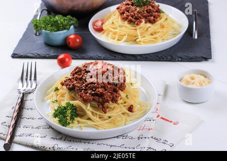 Healthy Plate of Italian Spaghetti Topped with a Tasty Tomato and Ground Beef Bolognese Sauce and Fresh Parsley on a White Wooden Table Stock Photo