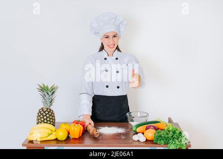 Chef woman holding bread rolling pin with thumb up, Smiling chef woman holding rolling pin on vegetable table, Concept of chef woman holding bread Stock Photo
