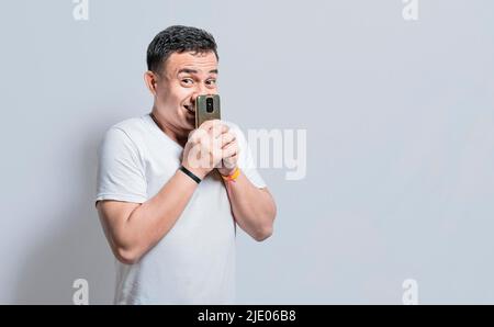 Attractive young man smiling with his cell phone, Attractive person smiling at the camera while holding his cell phone on isolated background, Young Stock Photo