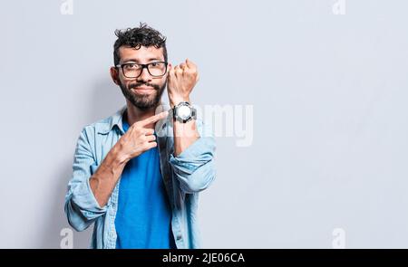 Person pointing at his watch looking at the camera. Friendly man pointing his wrist watch on isolated background, smiling person pointing finger at Stock Photo