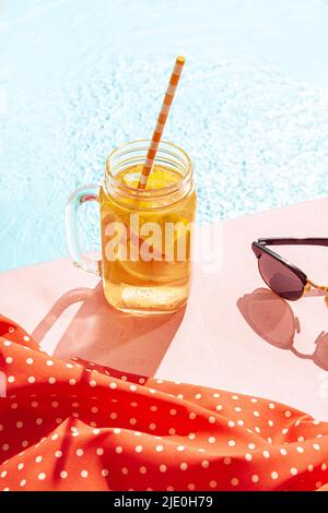 Cold drink on a hot summer day. Cocktail glass near swimming pool over blue sky background. Vacation, happiness, summer vibes and ad concept. Retro Stock Photo