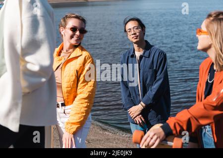 young asian man looking at camera near happy friends on riverside Stock Photo