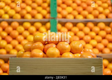 Wooden box with a stack of tangerines and unfocused tangerines background. Stock Photo