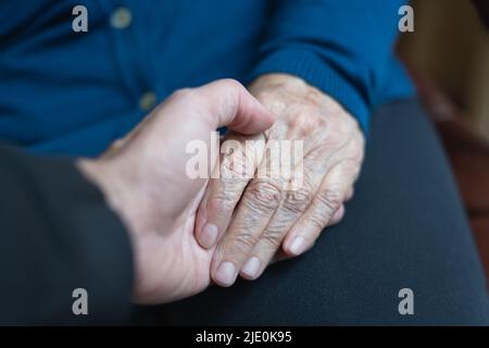 Young man's hand holding older woman's hand in caring and helping attitude. Stock Photo