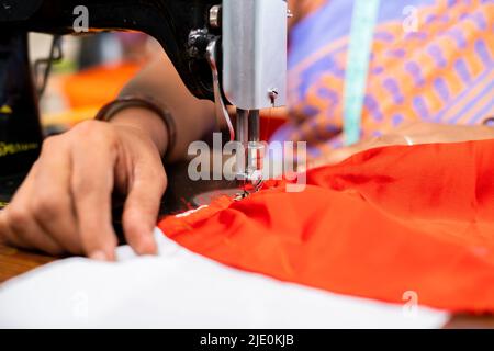 close up, hands of Indian woman at garments busy tailoring or stitching using sewing machine - concept of job, expertise and small home business. Stock Photo