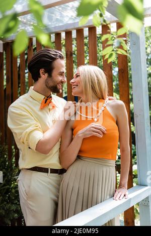 side view of stylish man wearing necklace on stylish girlfriend on terrace of cafe Stock Photo