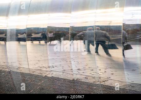 Sheffield, UK – 13 November 2021: Passersby walking towards the train station reflected in the curved metal wall of The Cutting Edge sculpture, Sheaf Stock Photo
