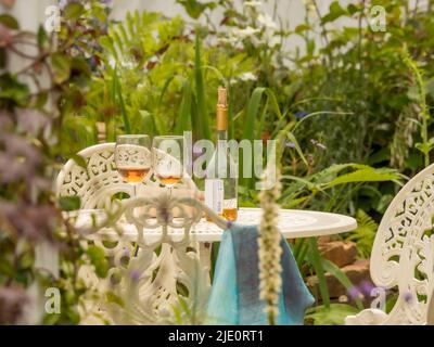 Bottle of wine along with 2 glasses and paperback book on a white cast iron garden table. Stock Photo