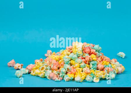 Multi-colored popcorn is scattered on a blue background. Colorful beautiful sweet dessert. Stock Photo
