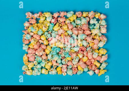 Multicolored popcorn in the shape of a square on a blue background. Colorful beautiful sweet dessert. Stock Photo