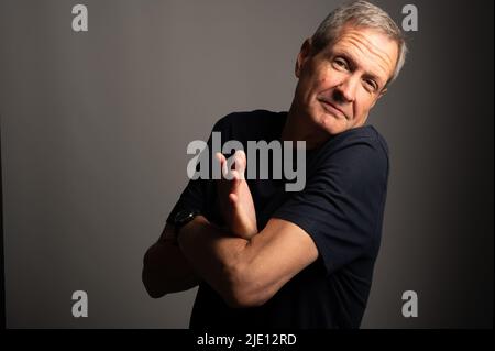 Mature man shrugging, on a grey background with copy space Stock Photo