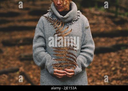 Save the planet and earth's day concept lifestyle. Portrait of woman holding dry big leaf in the woods. Autumn color and leisure park activity concept Stock Photo