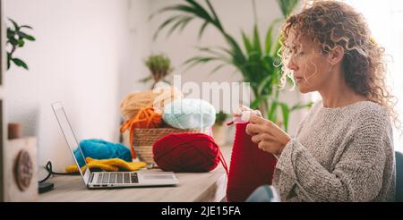 Woman at home in leisure activity learning from online class to knit work. Female people using laptop for her hobby or alternative work. Middle age la Stock Photo