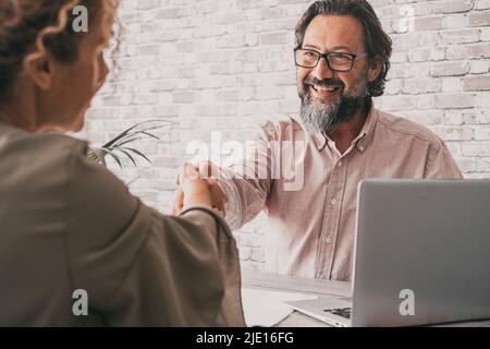 Couple of seller and buyer holding hands to sign an agreement. Confident professional business man give hand to woman client sitting at the desk in th Stock Photo