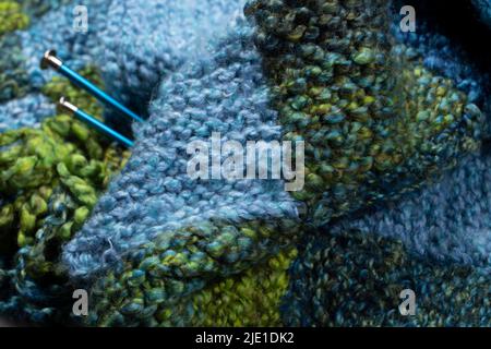 A knitting closeup of a wool quilted blanket with needles with blue and green squares. Stock Photo
