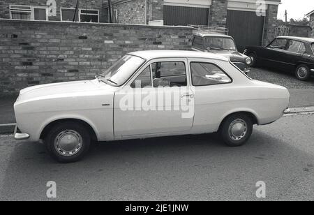 1970, historical, a little girl sitting in the passenger seat of a two-door Ford Escort 'De Luxe' parked outside in a street, on a housing estate, with her head just in vision, England, UK. The Ford Escort, produced from 1968 to 2000, was one of the best selling cars in Britain. Stock Photo