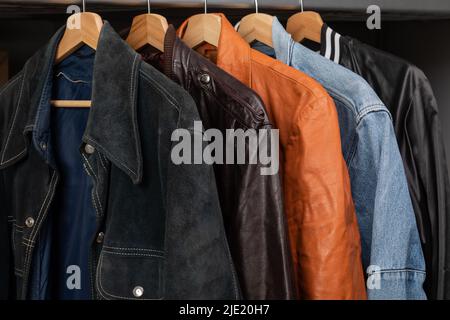 Various vintage suede leather and jeans jackets on hanger rack in a used goods store. Thrifting and sustainability in clothing concept Stock Photo
