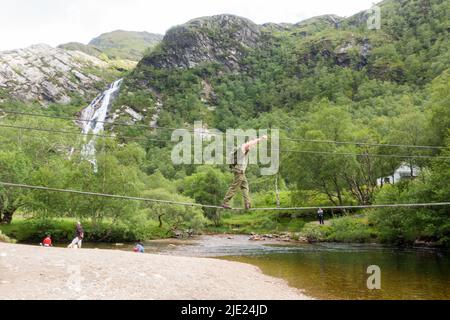 Man walking across Steall wire bridge over Water of Nevis river with Steall Falls Stock Photo