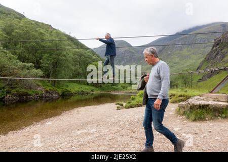 Man walking across Steall wire bridge over Water of Nevis river with Steall Falls Stock Photo