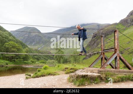 Man walking across Steall wire bridge over Water of Nevis river with Steall Falls Stock Photo