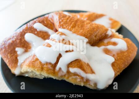 Danish Pastry with partial icing sugar applied isolated on a black plate in wooden table Stock Photo