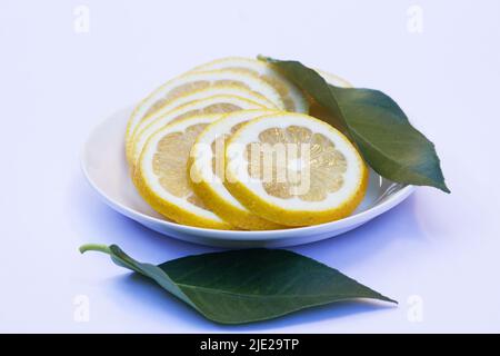 Sliced lemons and green leaves on a white plate isolated on white background Stock Photo
