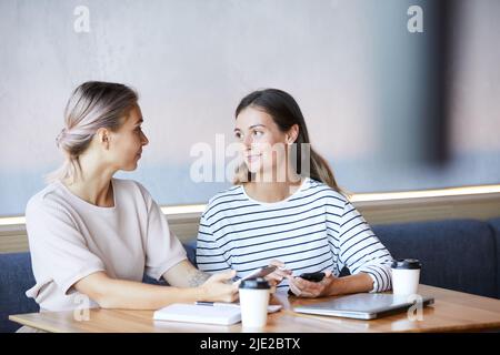 Content young women sitting at table in cafe and using gadgets while discussing ideas for startup project Stock Photo