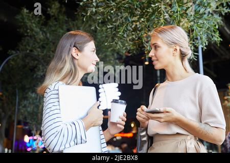 Content attractive young women in casual clothing standing at dark street and discussing business ideas Stock Photo