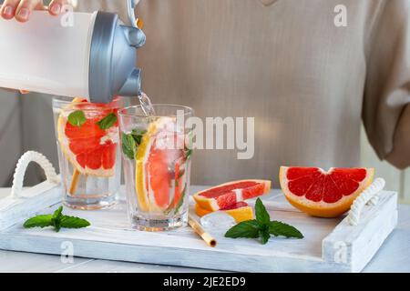 Girl cooking summer refreshing fruit cocktail with grapefruit slices and mint. Stock Photo