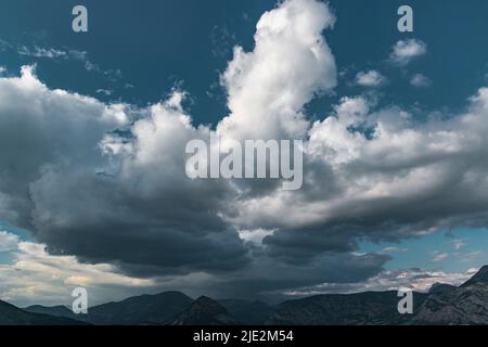 Scenic rain clouds over mountain tops. Bug cumulus clouds on the deep blue sky. Stock Photo