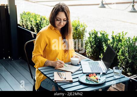 Mental health mood tracker, Woman sitting in street cafe and fills mood tracker in notepad Stock Photo