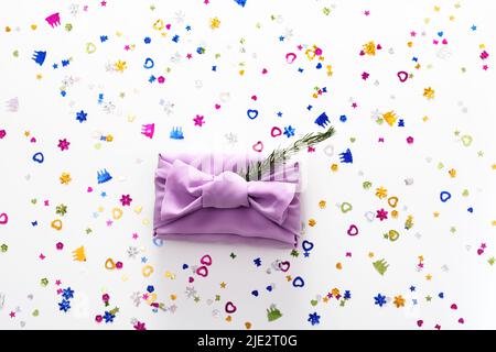Furoshiki Christmas gift wrapped in reusable fabric using environmentally friendly Japanese packaging technology. Christmas tree branches, shiny confetti on surface. Concept of zero waste. Copy space Stock Photo