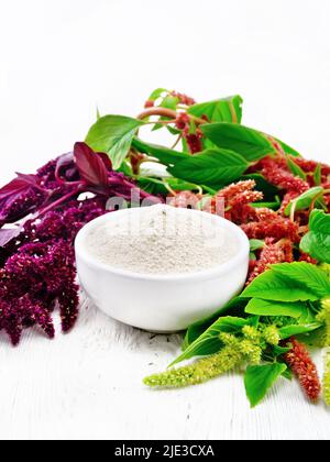 Amaranth flour in a bowl, brown, green and purple flowers of a plant on light wooden board background Stock Photo