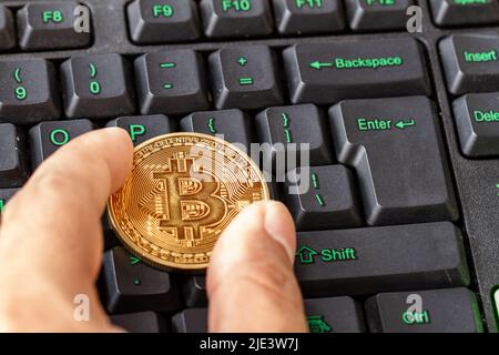 Hand holding bitcoin lying on computer keyboard, cryptocurrency for digital payment Stock Photo