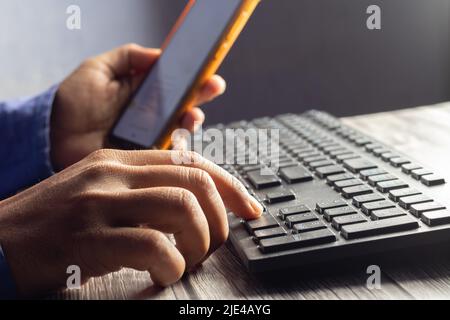 Selective focus on an Indian male hand using mobile phone to enter one time password in front of computer Stock Photo