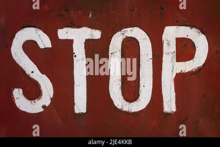 front view closeup of word stop written with white paint and capital letters brush typeface style on red rusted metallic plate texture Stock Photo