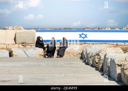 Arab women with Chador, sitting in the port of Old Jaffa with the Israeli flag in the background. The concept for peace. High quality photo Stock Photo