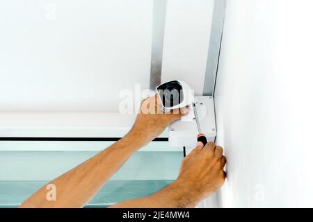 Technicians using a screwdriver to install  the CCTV cameras on the walls of the house for security purposes. Stock Photo