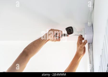 Technicians using a screwdriver to install  the CCTV cameras on the walls of the house for security purposes. Stock Photo