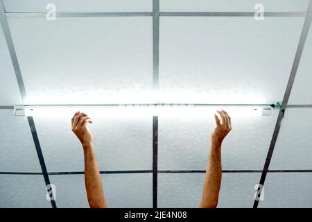 Close-up of a man's hand installing a long LED light bulb on the ceiling. Stock Photo