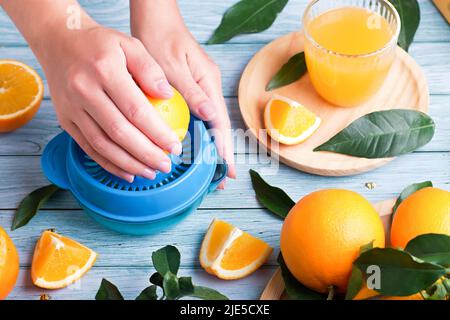Woman squeezing fresh orange juice on blue wooden table, top view Stock Photo