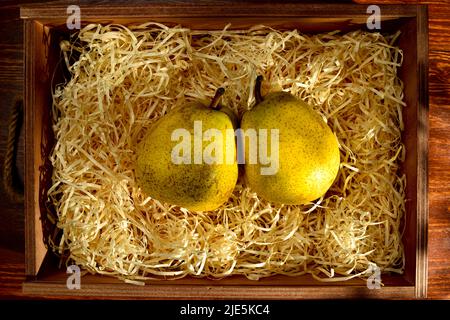 Two ripe pears in a box with shavings on a wooden table, close-up, top view. Stock Photo