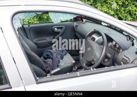 A car with its drivers side window smashed after being attacked by a thief. Shattered glass from the window is shown on the seats inside the insecure vehicle Stock Photo